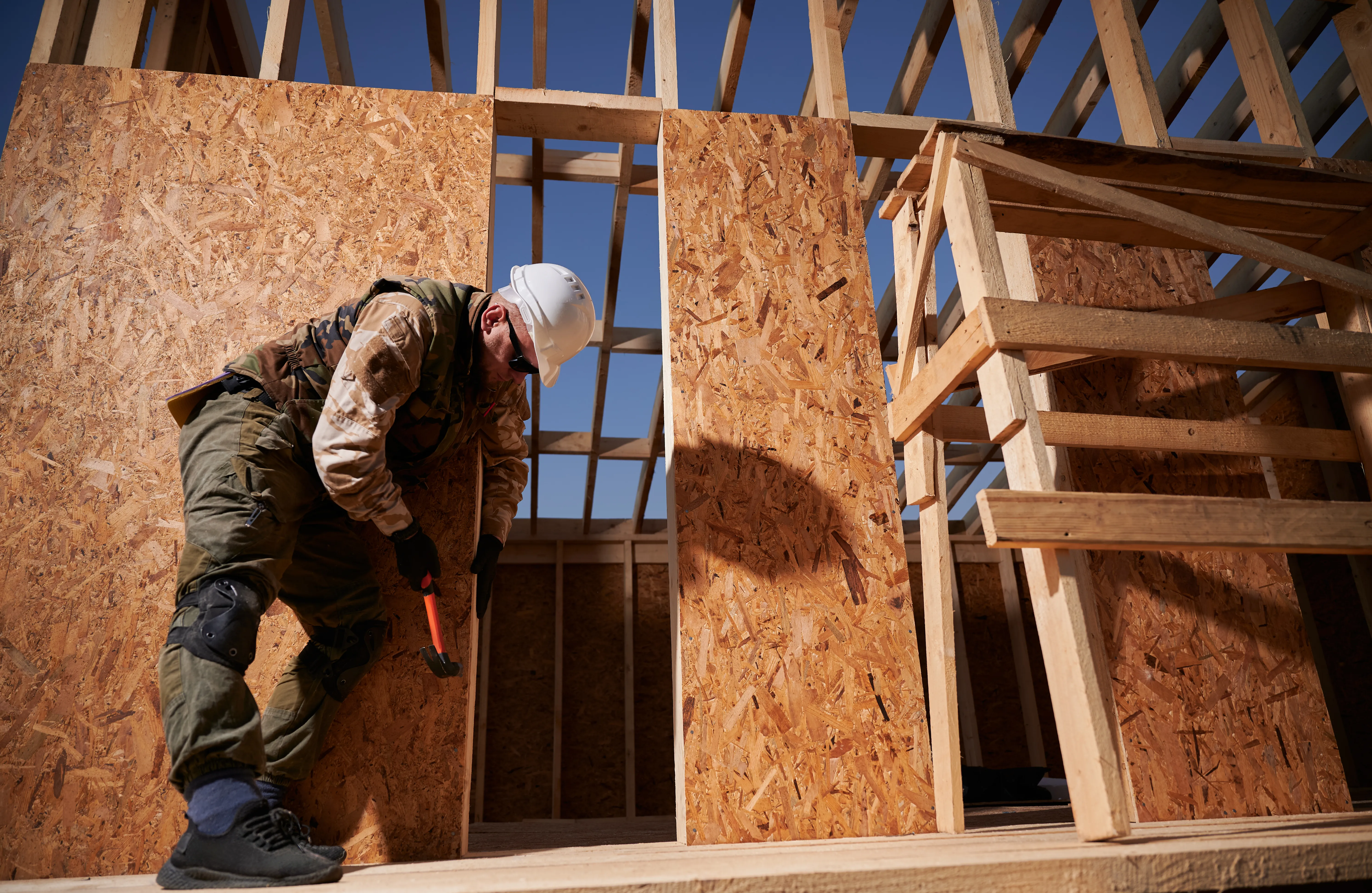 Carpenter hammering a nail into an OSB panel during ADU wood framing construction