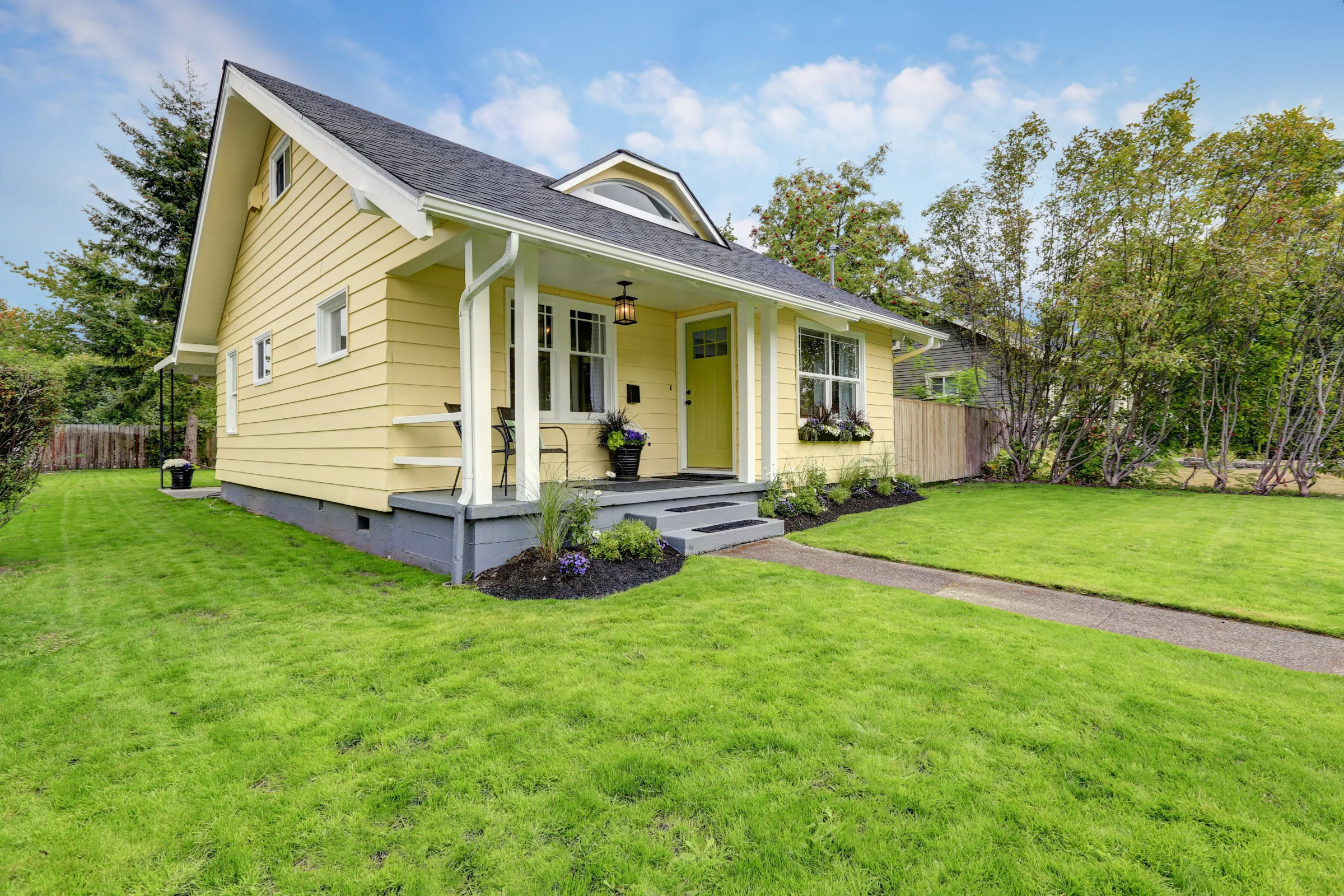 Custom ADU design build in Los Angeles featuring a classic backyard cottage with yellow siding, front porch, walkway, and landscaped lawn